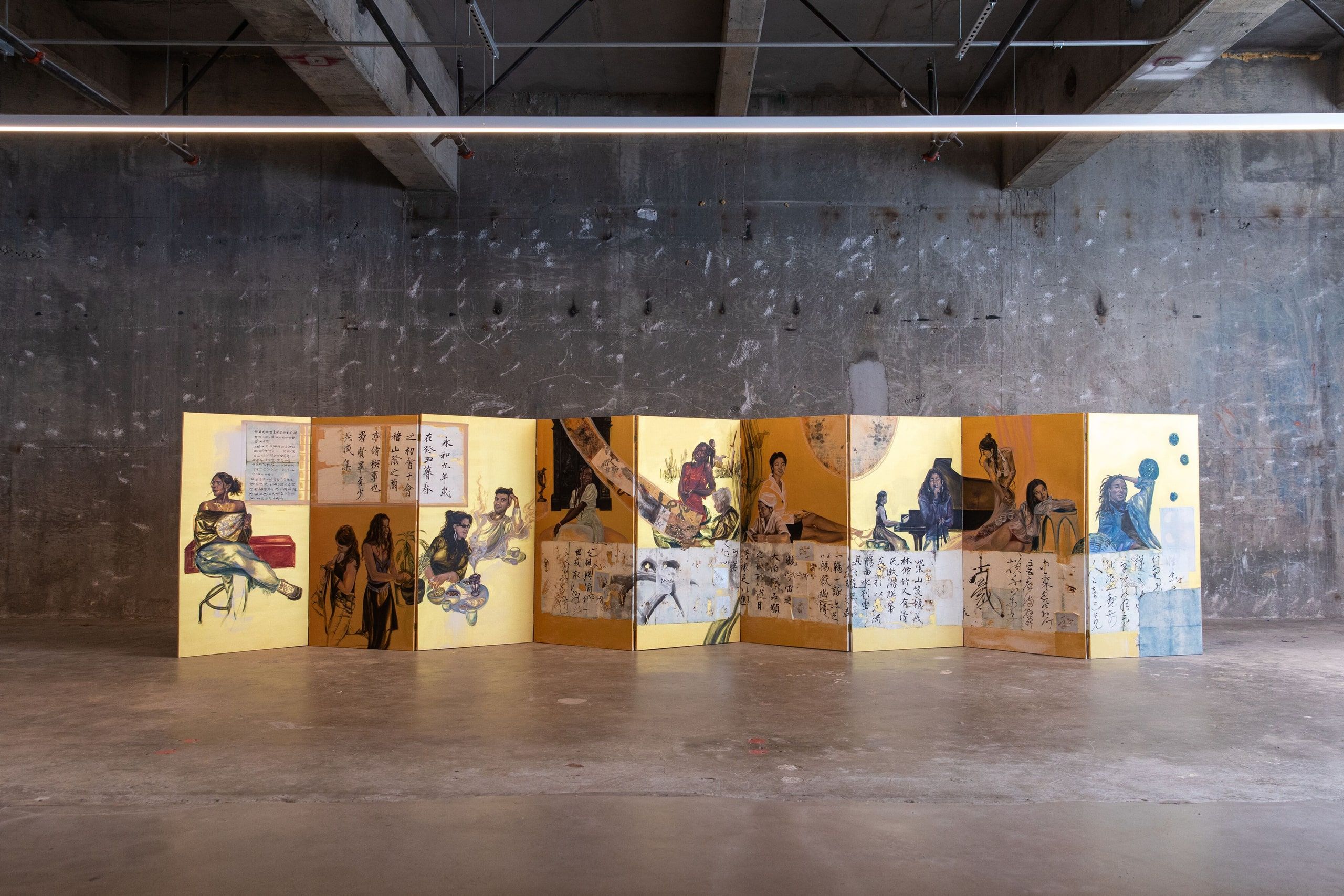 A large-scale installation of accordion-folded yellow panels with illustrated figures and handwritten text arranged in an industrial gallery space.