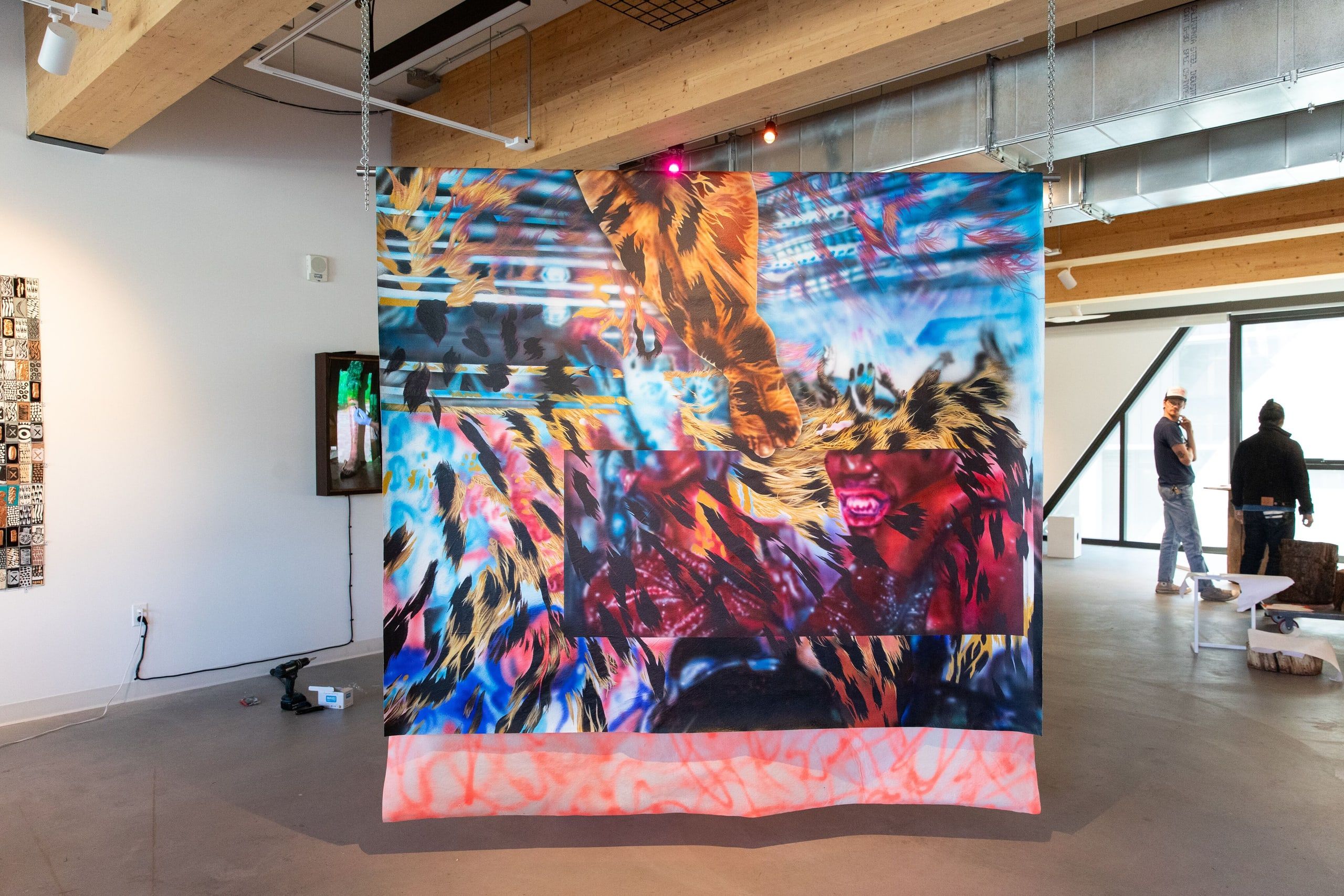 A vibrant large-scale digital projection displays abstract fiery patterns of reds, blues, and yellows on a curved screen in a modern gallery with visitors viewing the installation.